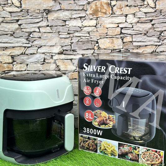 Silver Crest Air Fryer with a 8-liter capacity displayed alongside its packaging box. The appliance is green in color with a glass bowl visible and touch screen interface.